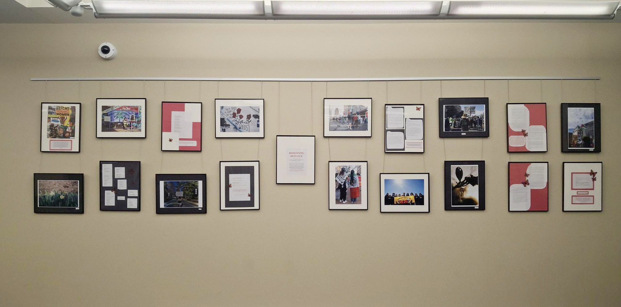 The exhibit wall displays 19 framed two-dimensional artworks and texts.