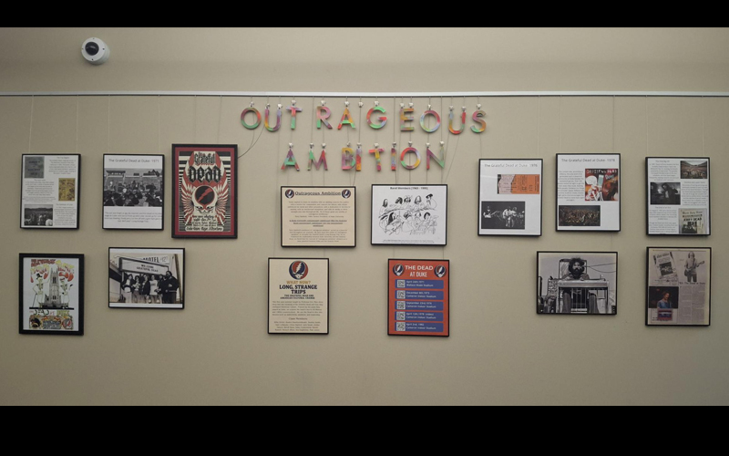 Exhibit wall displaying various exhibit frames and 'Outrageous Ambition' title panels.