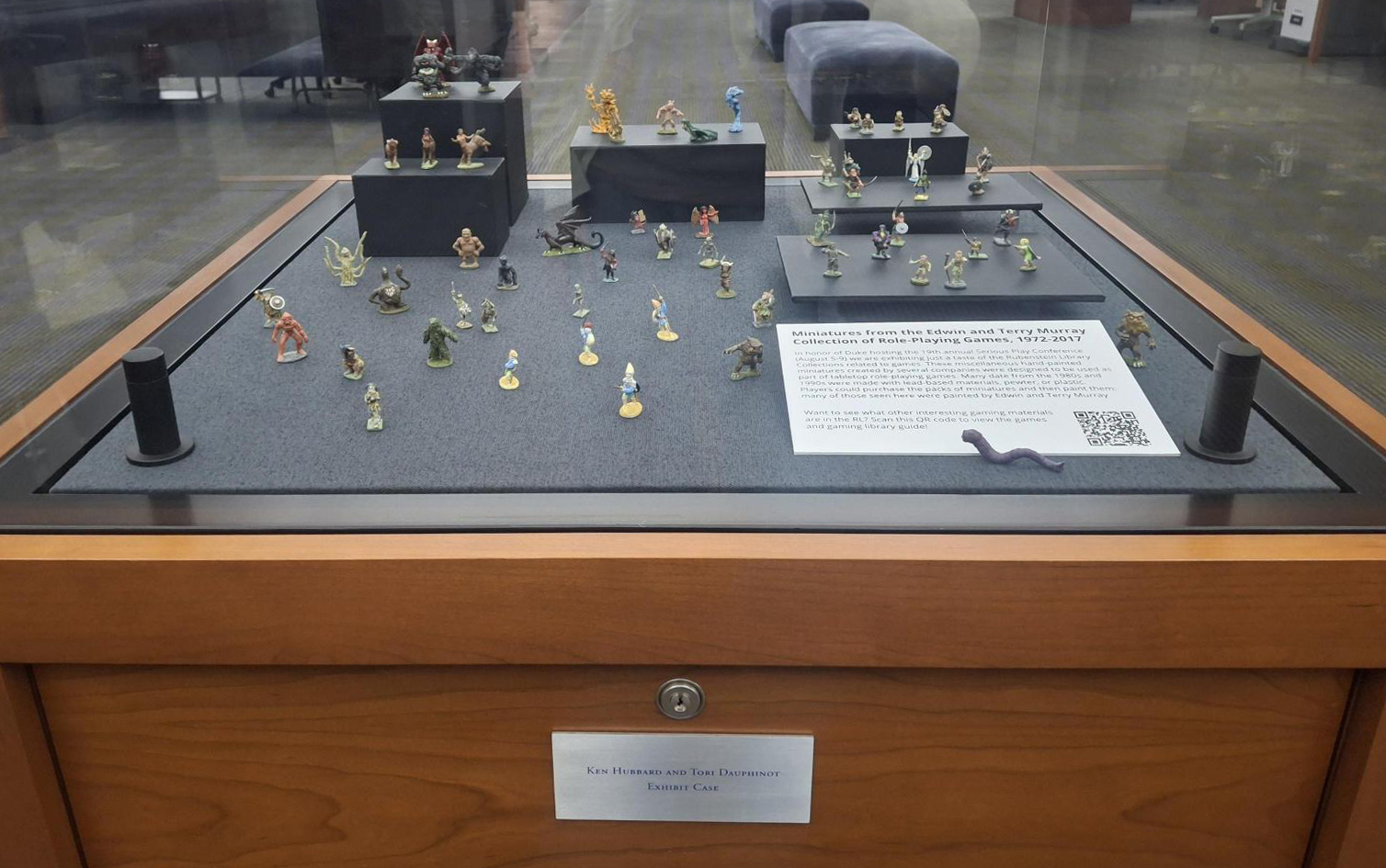 An exhibit case displaying miniature figures of fantasy characters and monsters, accompanied by a label.