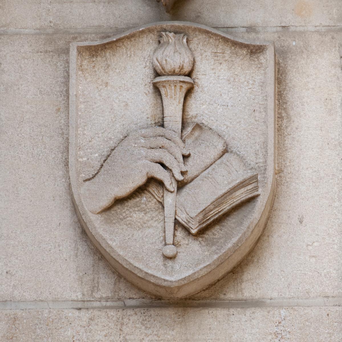 Stone shield from Rubenstein Library building showing an open book and a hand holding a torch